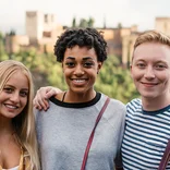 three students smiling with stone buildings and palm trees behind them