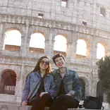 two students wearing jean jackets sitting on a ledge in front of the Colosseum in Rome, Italy