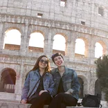 two students wearing jean jackets sitting on a ledge in front of the Colosseum in Rome, Italy
