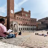 student leaning against a wall, reading in a plaza in Siena