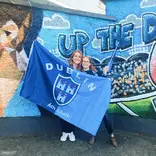 two student standing in front of a mural holding a large Dublin flag