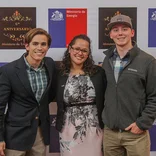 two students standing with their supervisor at an event