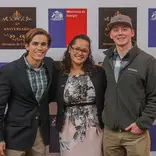 two students standing with their supervisor at an event