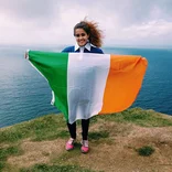 student holding an Irish flag near the Cliffs of Moher