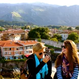 two students laughing at a lookout point with buildings and mountains behind them