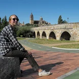 student resting on a rock with a bridge in the background in Salamanca