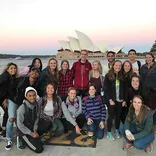 large group of students standing near the harbor with the Sydney Opera House behind them