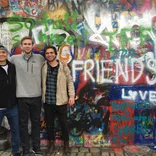 Students pose for a picture in front of artwork/graffiti that says 'friends'