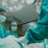 Medical interns wearing scrubs observe surgery in an operating theatre