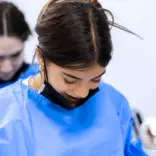 A teen medical intern wearing blue scrubs prepares to shadow medical professionals