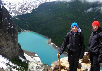 a girl stands on a ledge over looking a lake in the mountains