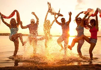 Happy people splashing in the ocean at sunset.