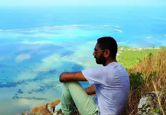 man sitting on hill above turquoise waters