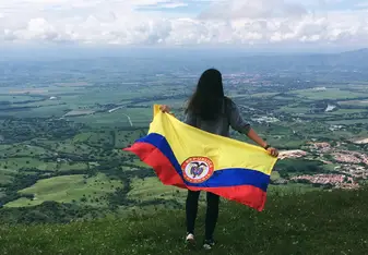 girl with Colombian flag standing on hill