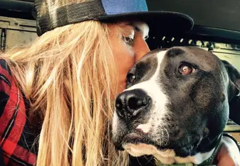 blode woman kissing black and white dog