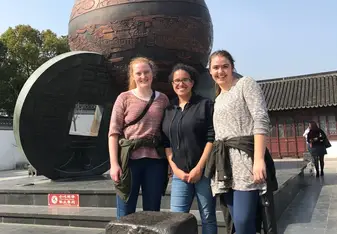 three woman having their picture taken on a huge round statue