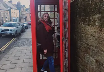 A lady poses inside a red telephone booth.