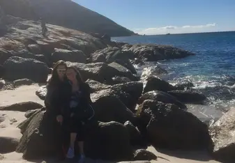 two women sitting on a big stone near a beach