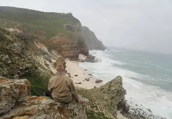 a man sitting a cliff near a sea