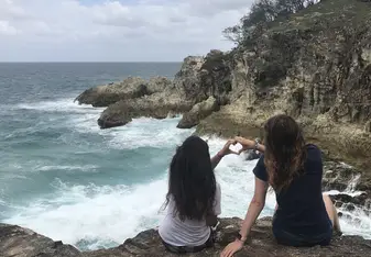 two women doing a heart sign while sitting on a seashore