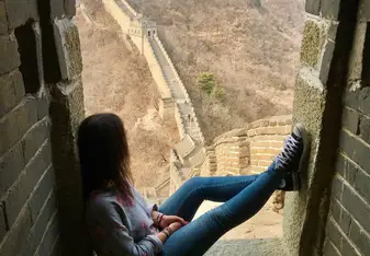 A girl sits at a spot at the Great Wall of China.