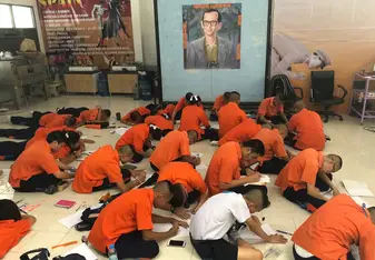 People wearing orange uniforms sit on the floor doing a school activity.