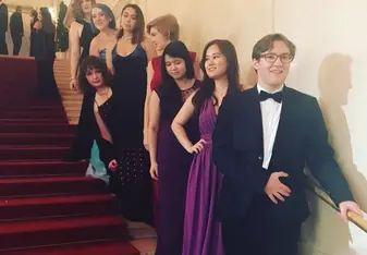People in formal suit and gowns pose at stairs.