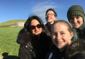 A field trip to Newgrange, featuring the reviewer, two classmates, and the instructor smiling with the ancient tomb in the background