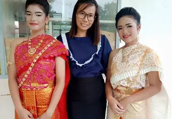 A woman posing with two younger women in traditional Thai costume.
