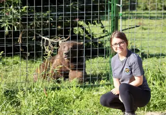 A woman poses for a photo near a caged bear.