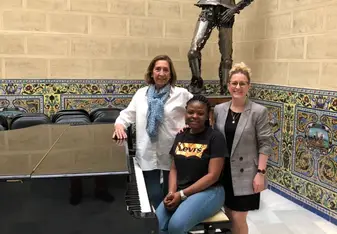 Three women posing near a piano.