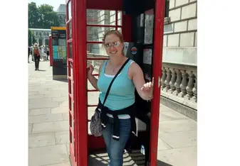 A woman poses inside a red telephone booth.