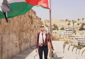 Me standing under a Jordanian flag on top of the Roman Amphitheatre in Amman, Jordan