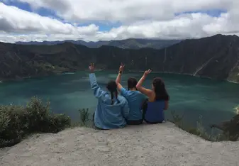Three girls sit on the edge of a crater within a volcano 