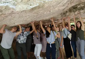 Group of students standing under a rock pretending to hold it up with shocked and strained expressions on their faces