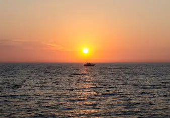 Sunrise over the coast of Ortigia with a boat crossing in front of the sun