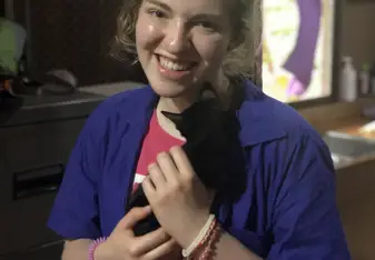 A female young adult in a blue veterinary lab coat holds a kitten in an Elephant Nature Park cat clinic.