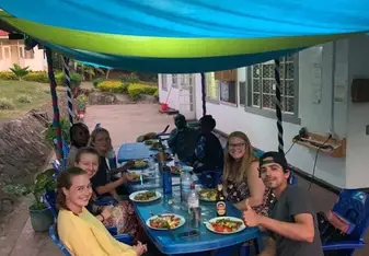 (group of people sitting around outdoor table, smiling with barbecue food)