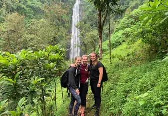 (three girls in lush green jungle, with big waterfall in the background)