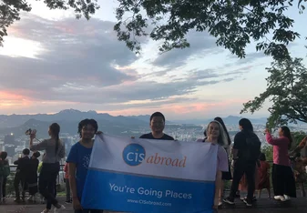 Three people holding a CISabroad flag posing against the sunset at Seoul Tower