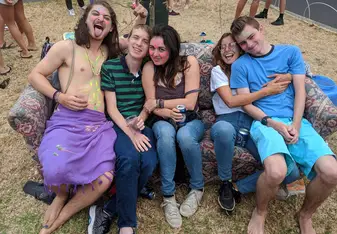 A group of friends laughing and sitting on a bench at a party.