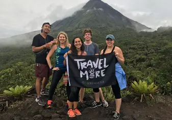 Standing in front of the Arenal volcano with the four other volunteers I lived with on a weekend adventure. We are holding a flag from the company Serengetee, that reads "Travel More."
