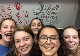Team members are standing and smiling in front of a wall on which there is a painting of a turtle, made by hand-prints.