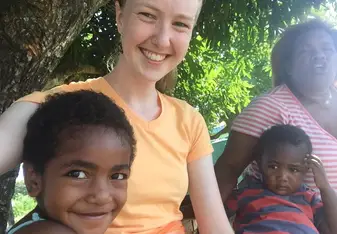 Zoe is sitting with Anna (small girl in the front), both are smiling. In the background Tutubai (small boy) looks unimpressed, while Ima laughs.