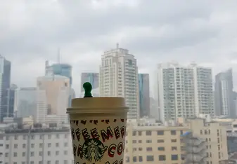 Holding a Starbucks cup in front of a window on the high floor of a building, overlooking Huangpu