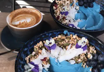 A beautifully done smoothie bowl with a cup of coffee.