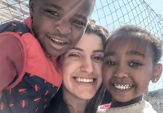Voluntária abraçada com duas crianças sorridentes.