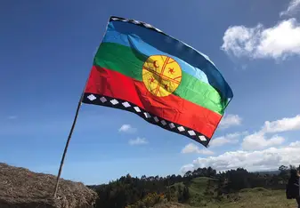 A mapuche flag flies against a blue sky