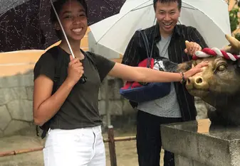 Grace touching a bull statue at Dazaifu shrine with her host dad in the background