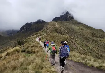 Students walk along green, grassy path towards mountain peak.
